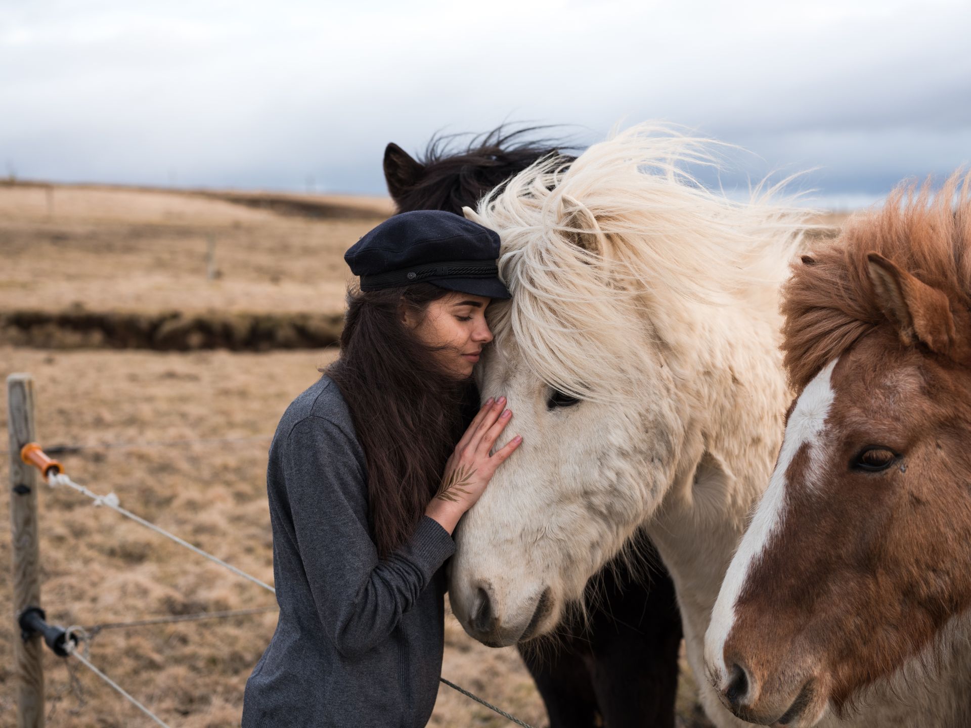 Vrouw leunt met gesloten ogen tegen het hoofd van een wit paard